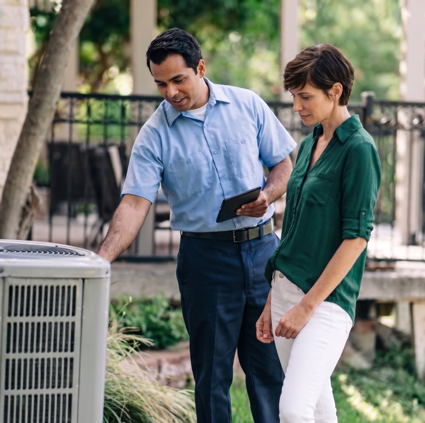 HVAC technician with a tablet reviewing an outdoor AC unit with a homeowner