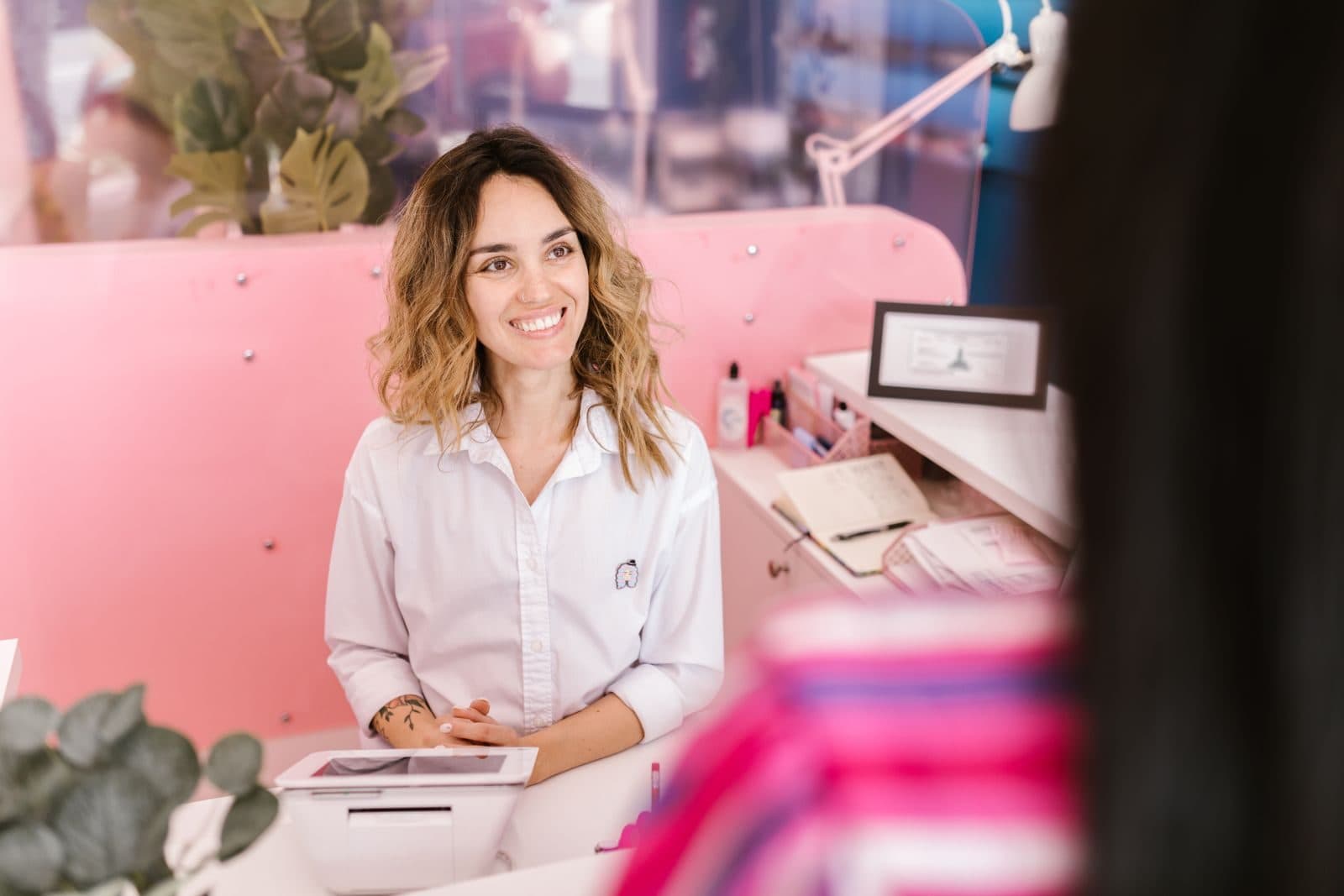 A smiling front-desk manager greets a customer across a reception counter.