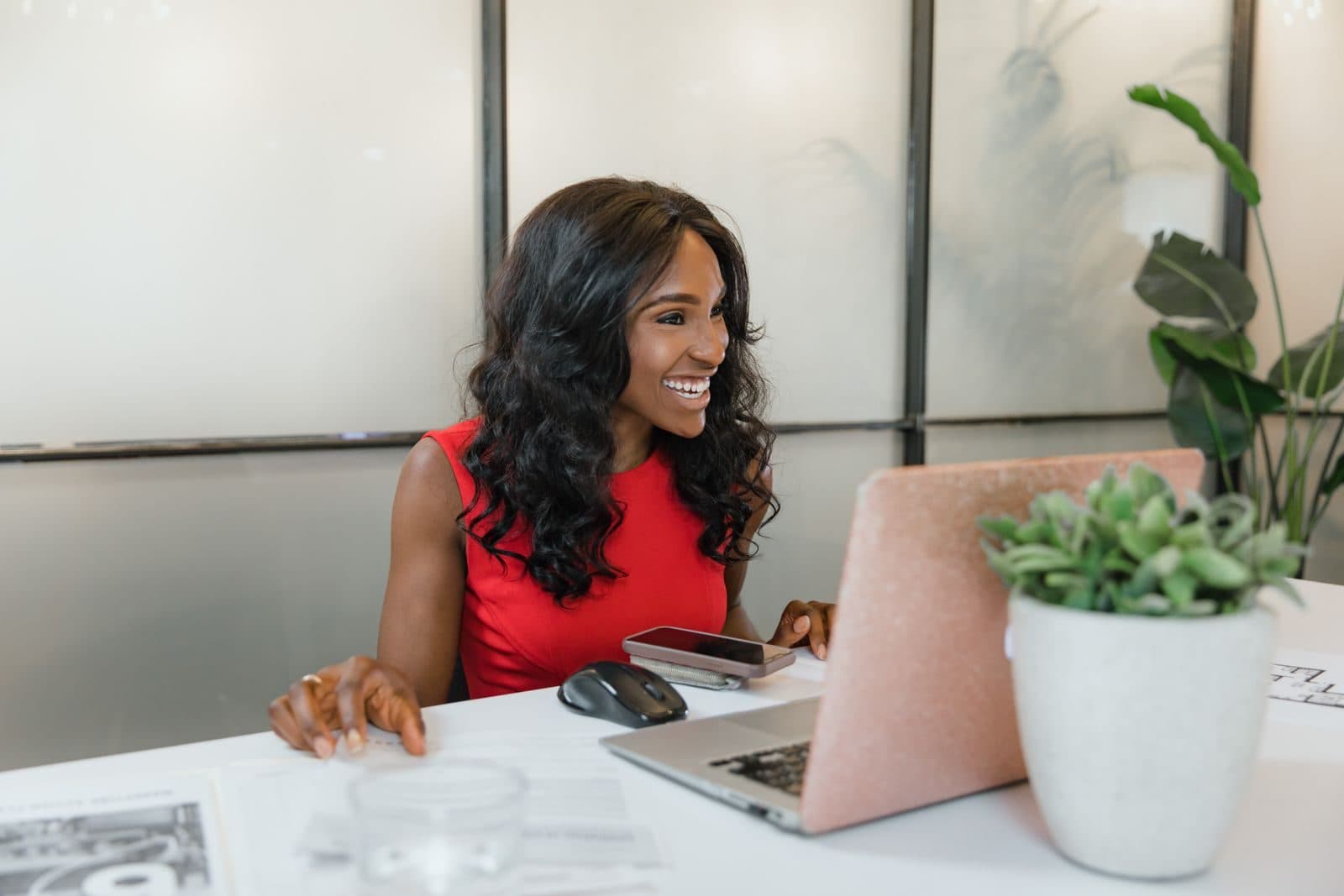 A smiling business owner in a red top works at her laptop in a bright office.
