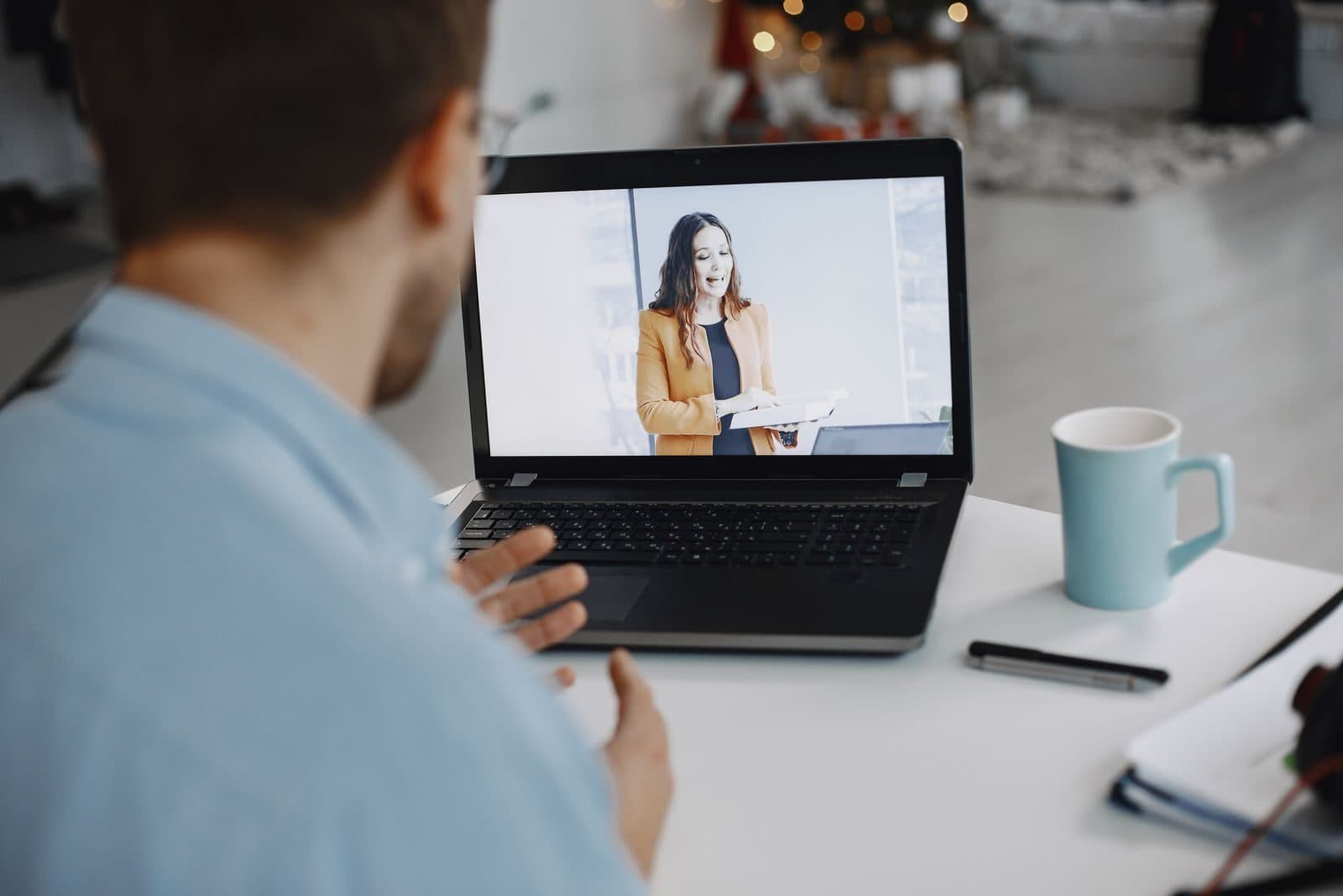 A man talks with a smiling colleague on a laptop video call at a bright desk.