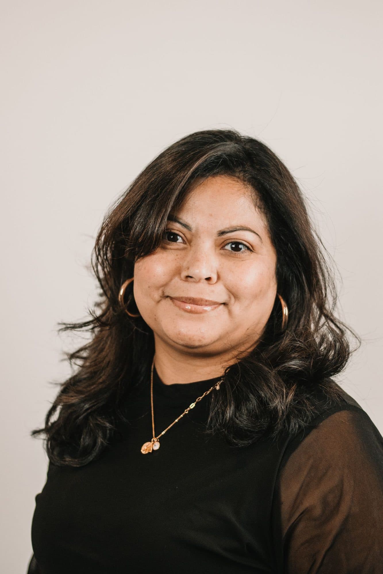 Portrait of a confident woman with shoulder-length dark hair against a light backdrop.